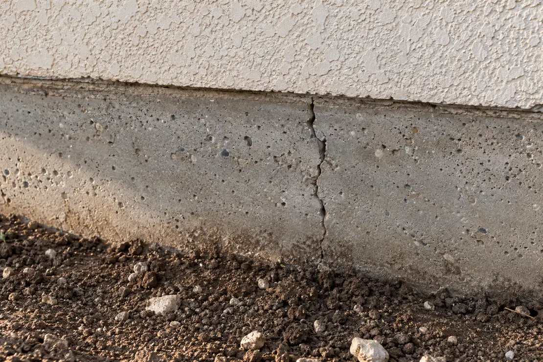 Crack along the exposed edge of a concrete slab beside dry, dark soil